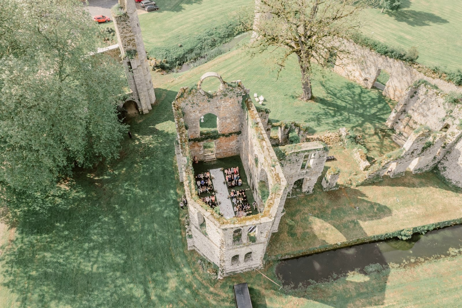 Cérémonie laïque au Château du Vivier : une vue aérienne sur une abbaye historique Vue aérienne du Château du Vivier lors d'une cérémonie laïque, les invités réunis dans les ruines majestueuses d'une abbaye sans toit, entourées de verdure