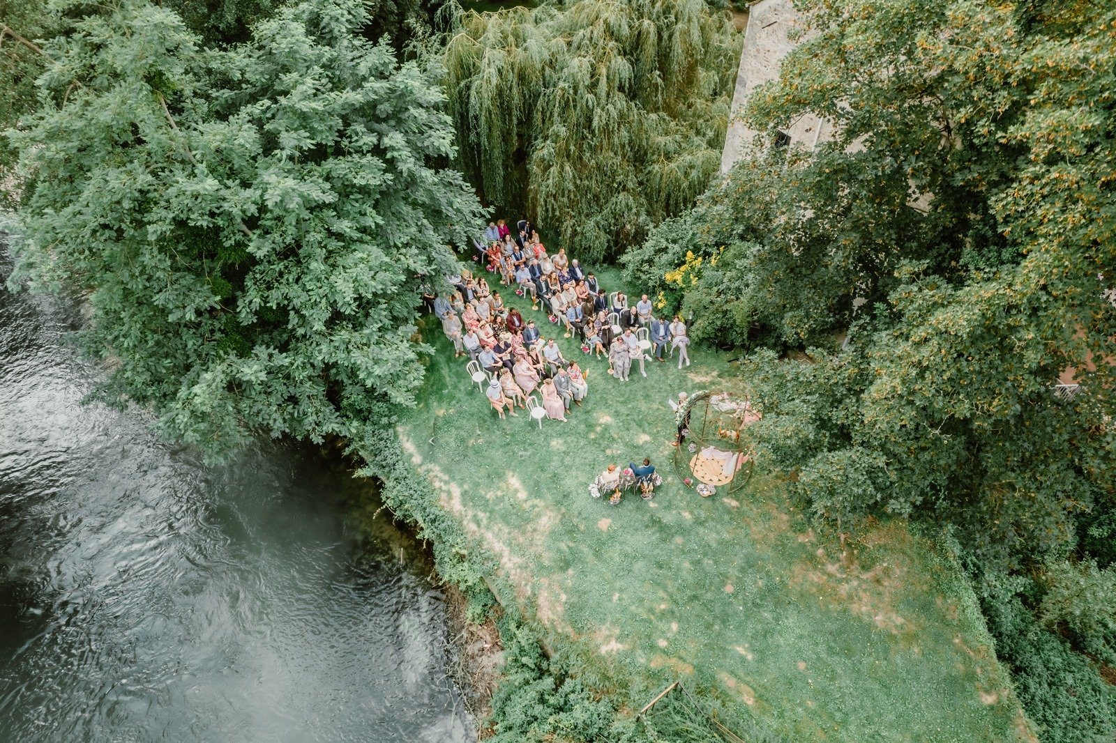 Vue aérienne d'une cérémonie laïque en pleine nature au Moulin de Pommeuse, dans une forêt entourée par une rivière, avec des invités rassemblés sous un décor champêtre